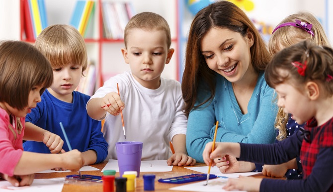Preschool-aged students painting at a table with their teacher