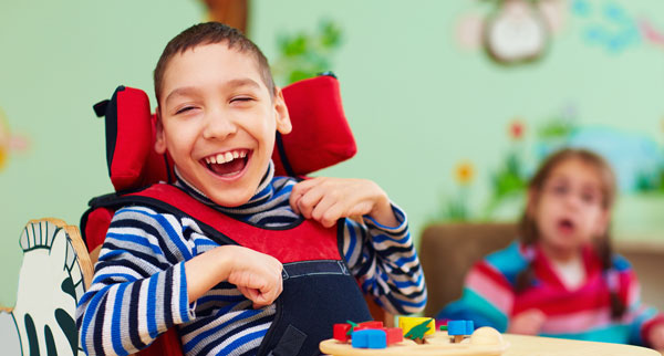 Boy in wheelchair smiling in a classroom with another child